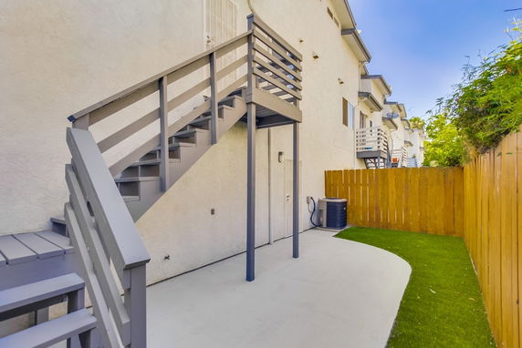 Side view of a multi-story building with external staircase and a fenced yard.