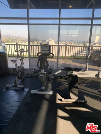 Indoor gym area with exercise machines near large windows.