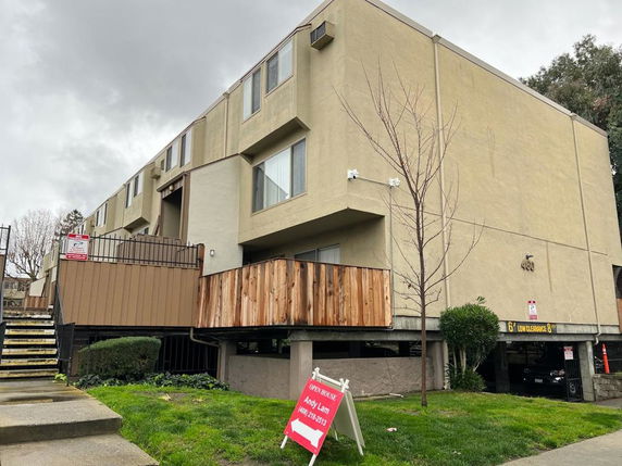 Front view of a multi-story apartment building with a gated entrance and partial wooden fencing.