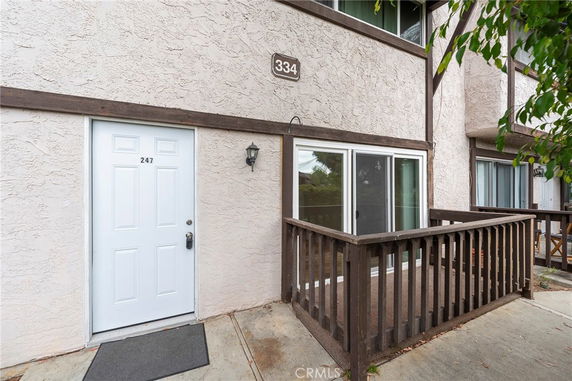 Front view of a building with a light-colored exterior, a white door marked '247', and a small fenced patio area.