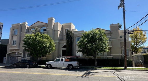 Front view of a multi-story building with trees and parked vehicles.