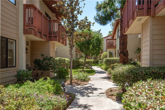 View of a sidewalk and landscaping between residential buildings with balconies.