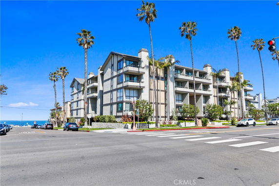 Front view of a multi-story residential building with balconies and palm trees nearby.