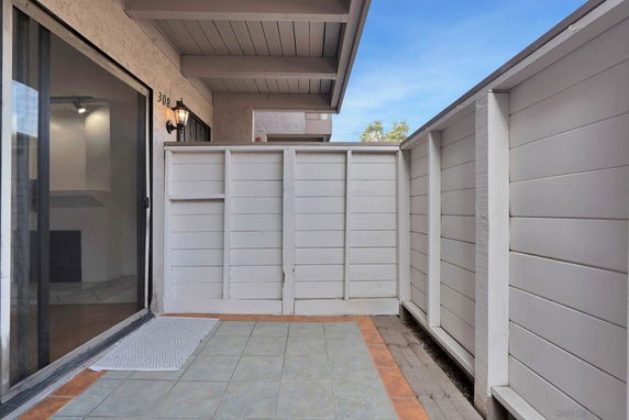 Outdoor area with tiled flooring and white fence walls, next to a building entry.