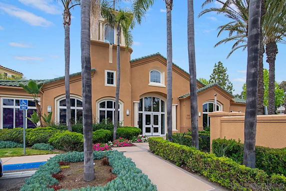 Front view of a building with large arched windows and a tall entrance, surrounded by palm trees and landscaping.