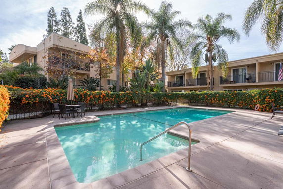 Outdoor swimming pool area with patio furniture and surrounding apartment buildings.