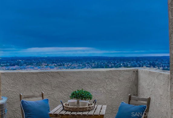 Panoramic view from a building balcony with a table and chairs, overlooking a cityscape.