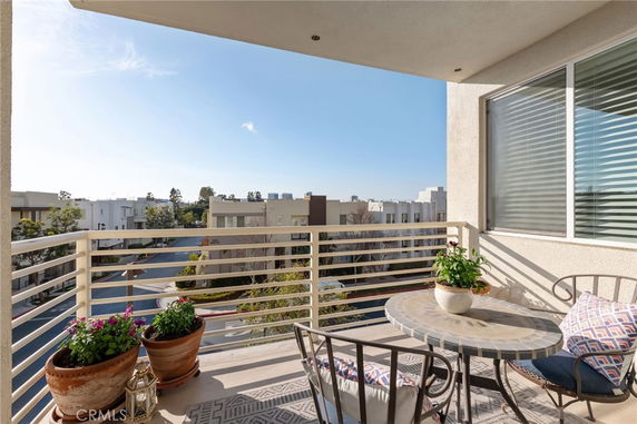 Outdoor patio with a small table and chairs offering a view of surrounding buildings and trees.
