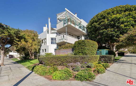 Front view of a modern multi-story residential building with balconies and surrounding greenery.