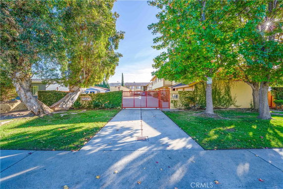 Front view of a house with a gated entrance and surrounding trees.
