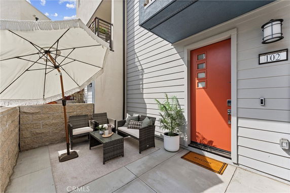 Front view of a house entrance with an orange door and outdoor seating area.