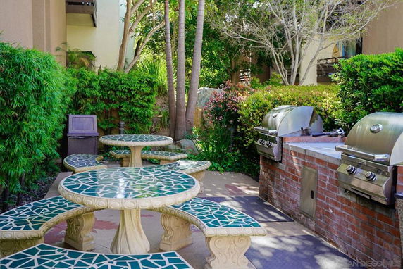 Outdoor area with mosaic tables, benches, and built-in grills surrounded by greenery.