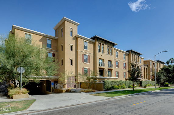Front view of a multi-story apartment building with balconies and a street in front.