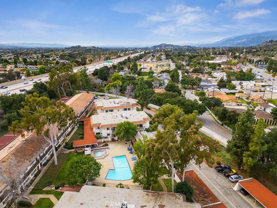 Aerial view of residential buildings with a swimming pool, surrounded by trees and roads.