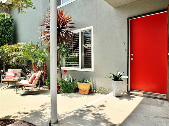 Front view of a house with a red door and plants on a patio.