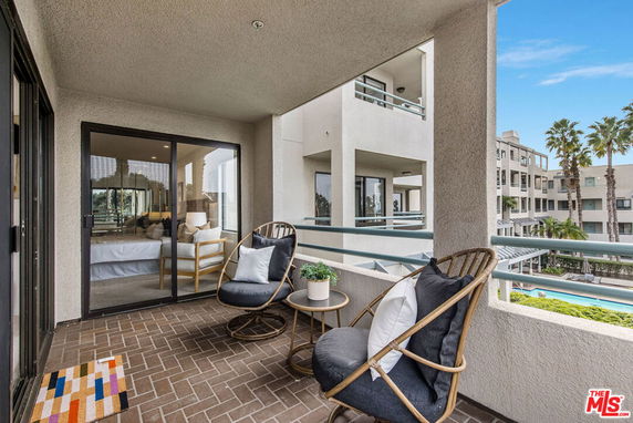 Balcony view with outdoor seating overlooking apartment buildings and palm trees.