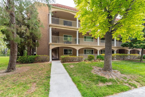 Front view of a three-story apartment building with balconies and a sidewalk leading up to it.