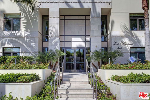 Front view of a modern multi-story building entrance with stairs and plants.