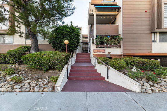 Front view of a multi-story apartment building with a staircase leading to the entrance.