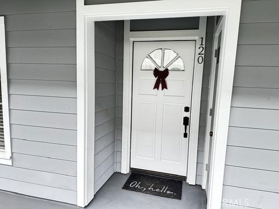 Front view of a grey house entrance with a white door, adorned with a red bow and a welcome mat.