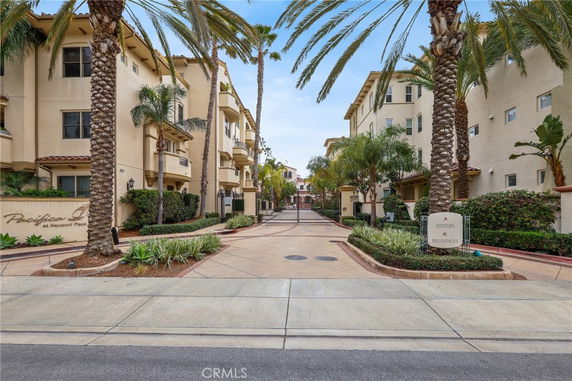 Front view of a multi-story residential complex with palm trees and gated entrance.