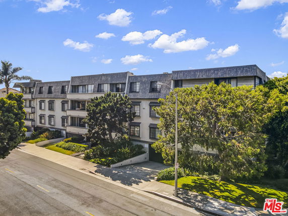 Front view of a multi-story building with a sloped roof and landscaped surroundings.