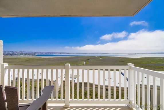 Panoramic view from a balcony overlooking a large open field and distant water body.