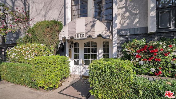 Front view of a building entrance with an awning and surrounding greenery.