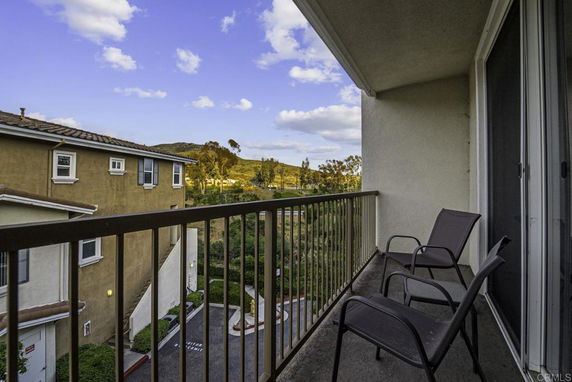 View from a balcony overlooking nearby buildings and a distant hillside under a blue sky.