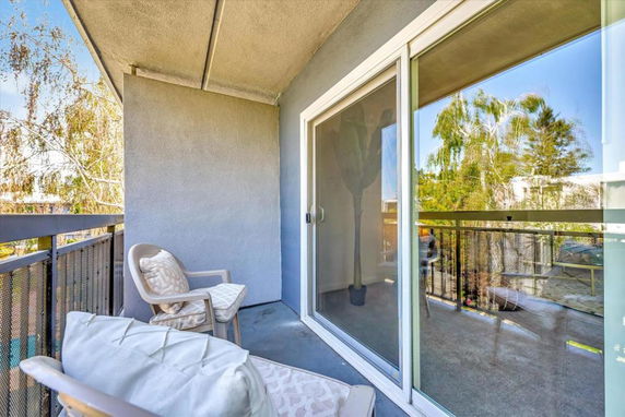 View from a small outdoor balcony with chairs and a railing, looking towards trees.