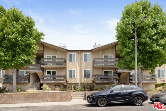 Front view of an apartment building with balconies and two trees in front.