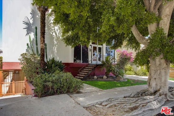 Front view of a house with stairs leading to the entrance and surrounded by trees and plants.