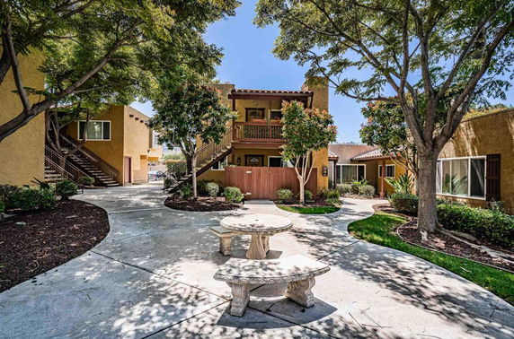 Front view of a multi-story residential building with outdoor staircases and trees in the courtyard.