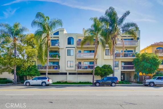 Front view of a multi-story apartment building with balconies and palm trees.