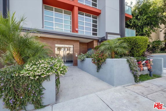 Front view of a modern multi-story building entrance with glass doors and landscaped planters.