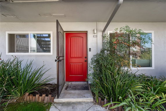 Front view of a building entrance with a red door and surrounding plants.