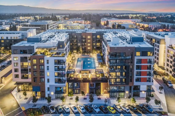 Front view of a modern multi-story apartment complex with a swimming pool on a central podium.