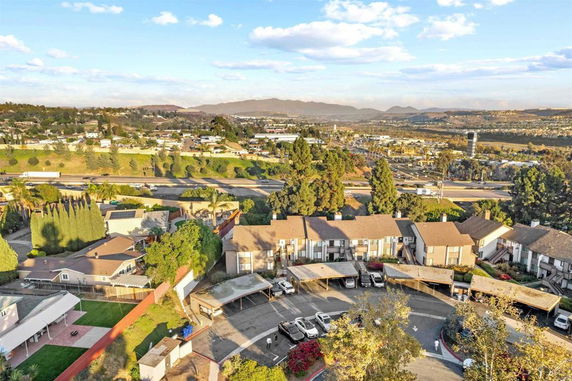 Aerial view of a residential area with multi-story houses and a parking area, surrounded by trees and hills.