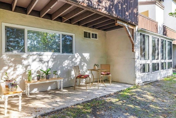 Patio area of a house with chairs and a table under a covered section.