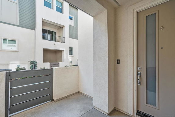 Entryway view of a modern multi-story building with a beige and gray exterior and balconies.