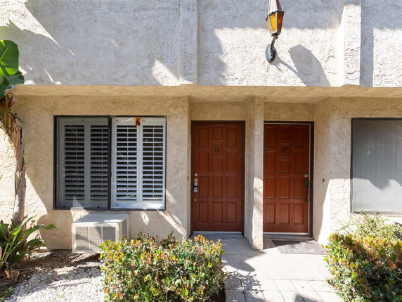 Front view of a building facade with two brown entrance doors and a window with shutters.