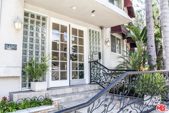 Front view of a building entrance with glass doors and decorative wrought iron railing on steps.