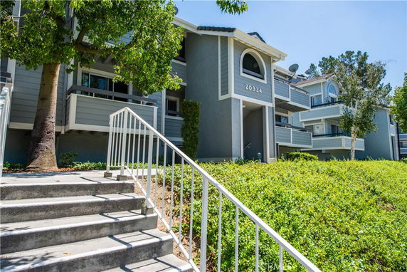Front view of a multi-story residential building with balconies and staircase entrance.