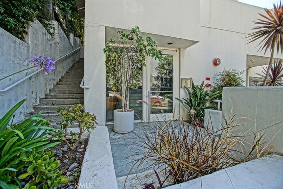 Front view of a building with a glass door entrance surrounded by plants and a staircase on the side.