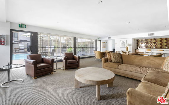 Interior view of a clubhouse with seating area, sofas, armchairs, and a pool visible outside.