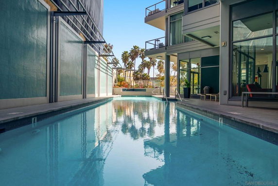 Outdoor swimming pool area adjacent to a modern building with large windows and balconies.
