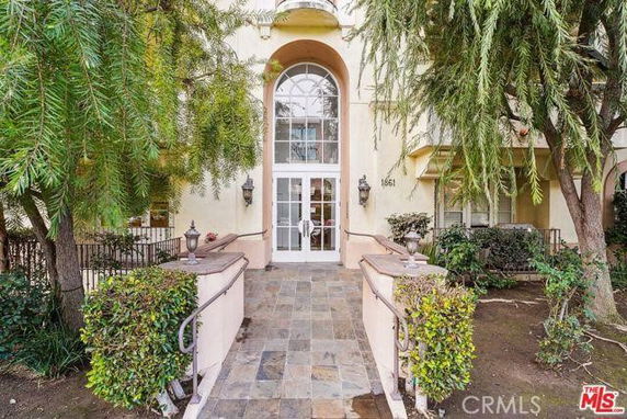 Front view of a multi-story building entrance with large arched windows and a tiled walkway.