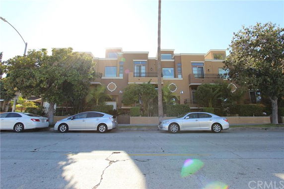 Front view of a multi-story residential building with balconies and parked cars in front.