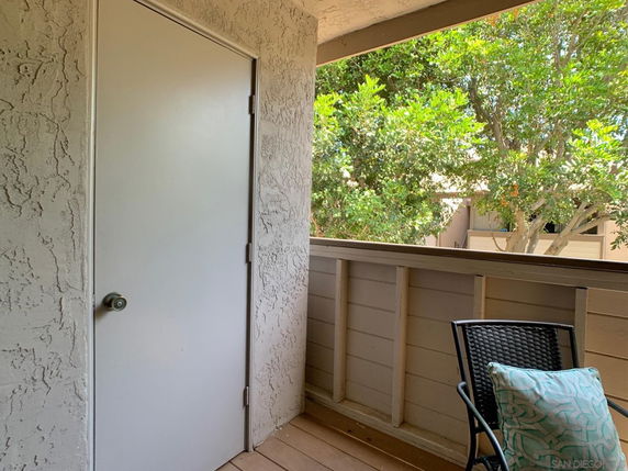 View from a small balcony with a chair and a pillow, overlooking trees and part of a building.