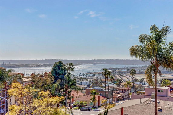 Panoramic view of a coastal city with buildings, water, and distant land.